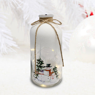 Frosted glass LED Christmas bottle glowing on tabletop with snowman family