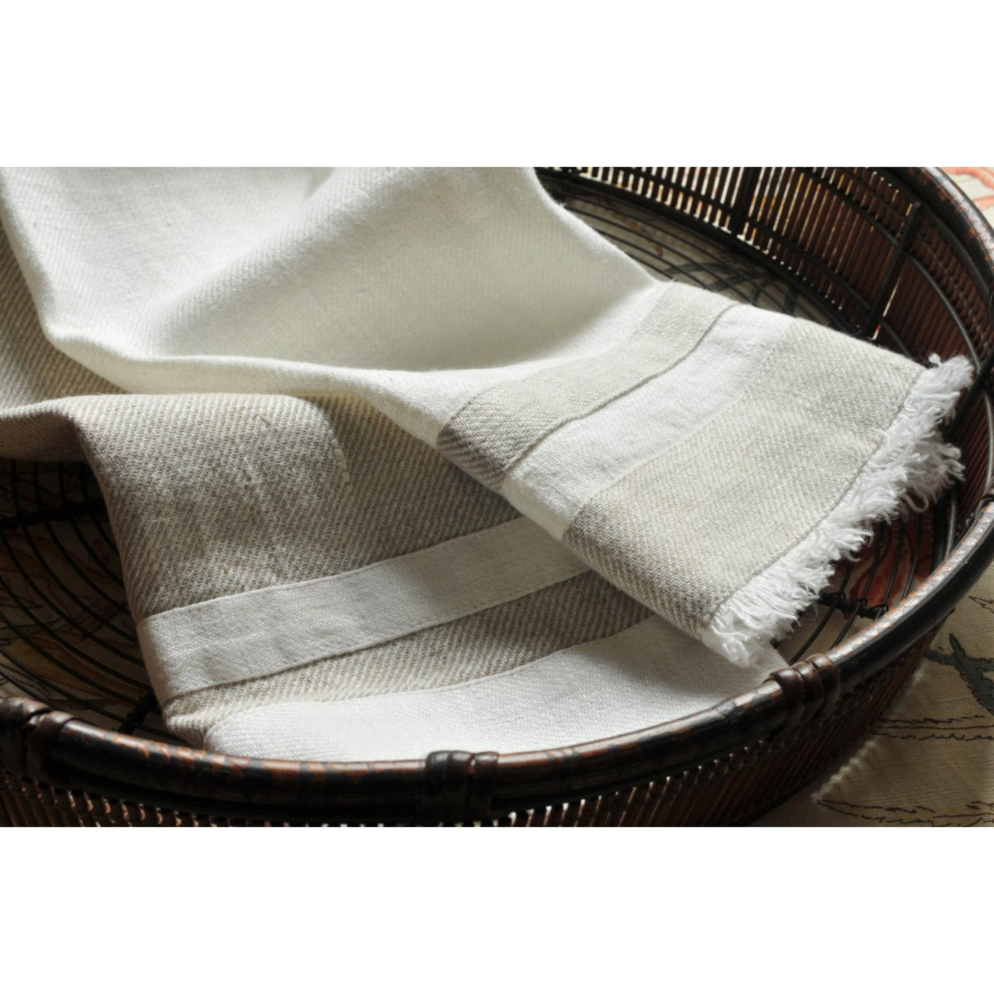 Lipari Linen Guest Towel: in basket. Beige with white stripes and fringed edges.