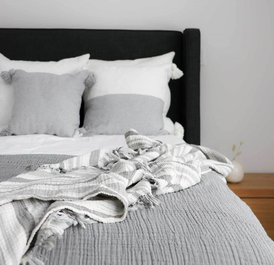 Pokoloko Moroccan pillows on bed. Half light grey with poms.