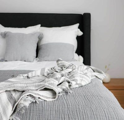 Pokoloko Moroccan pillows on bed. Half light grey with poms.