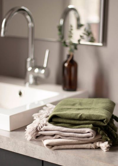 Turkish Hand Towel - Haven: Is made from the finest 100% Turkish cotton. 2 Oat towels and 1 green towel folded on bathroom sink.