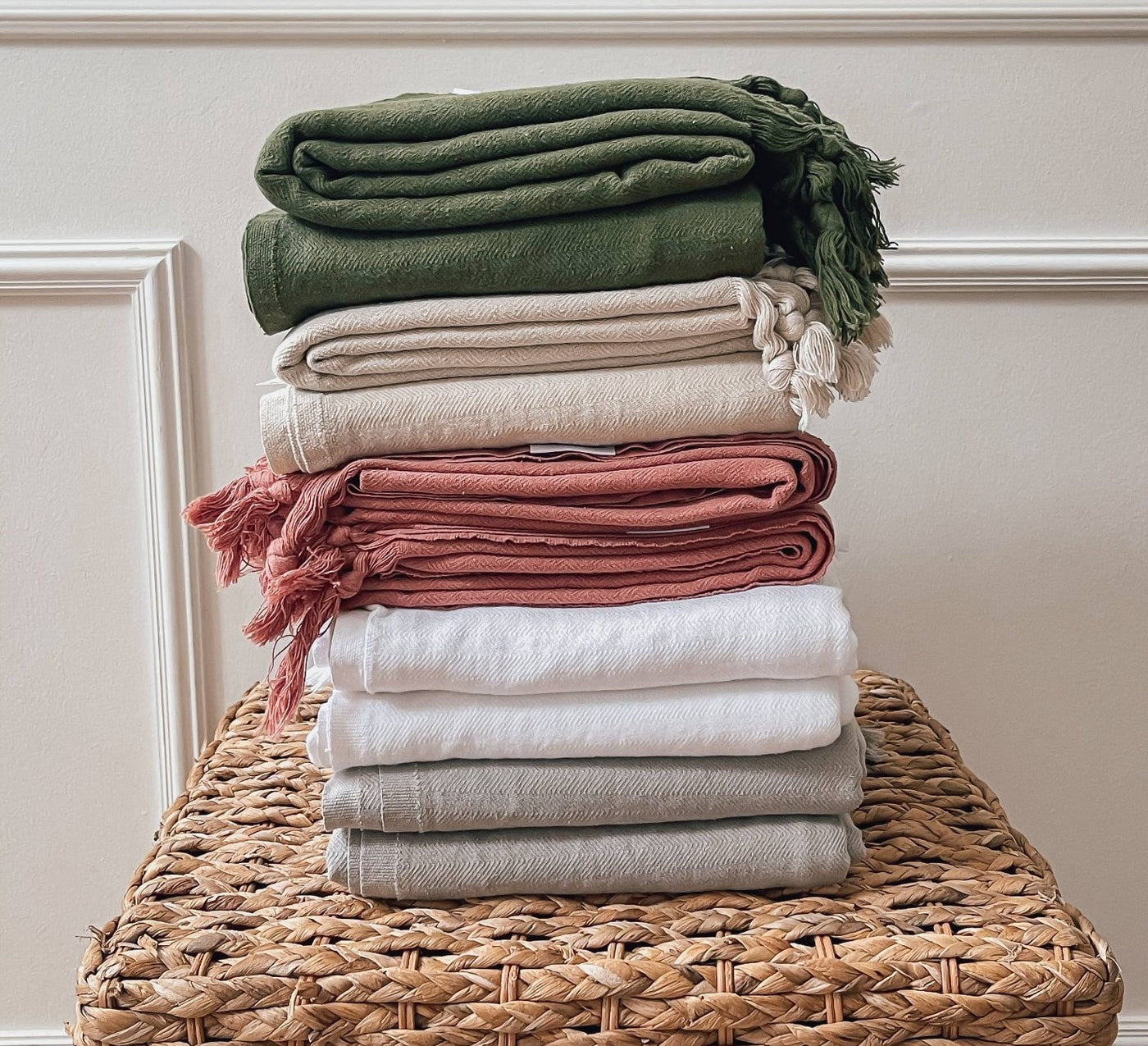 Turkish Towels: By House of Jude. Colors in green, oat, primrose, white and haven. Folded and stacked on Seagrass table.