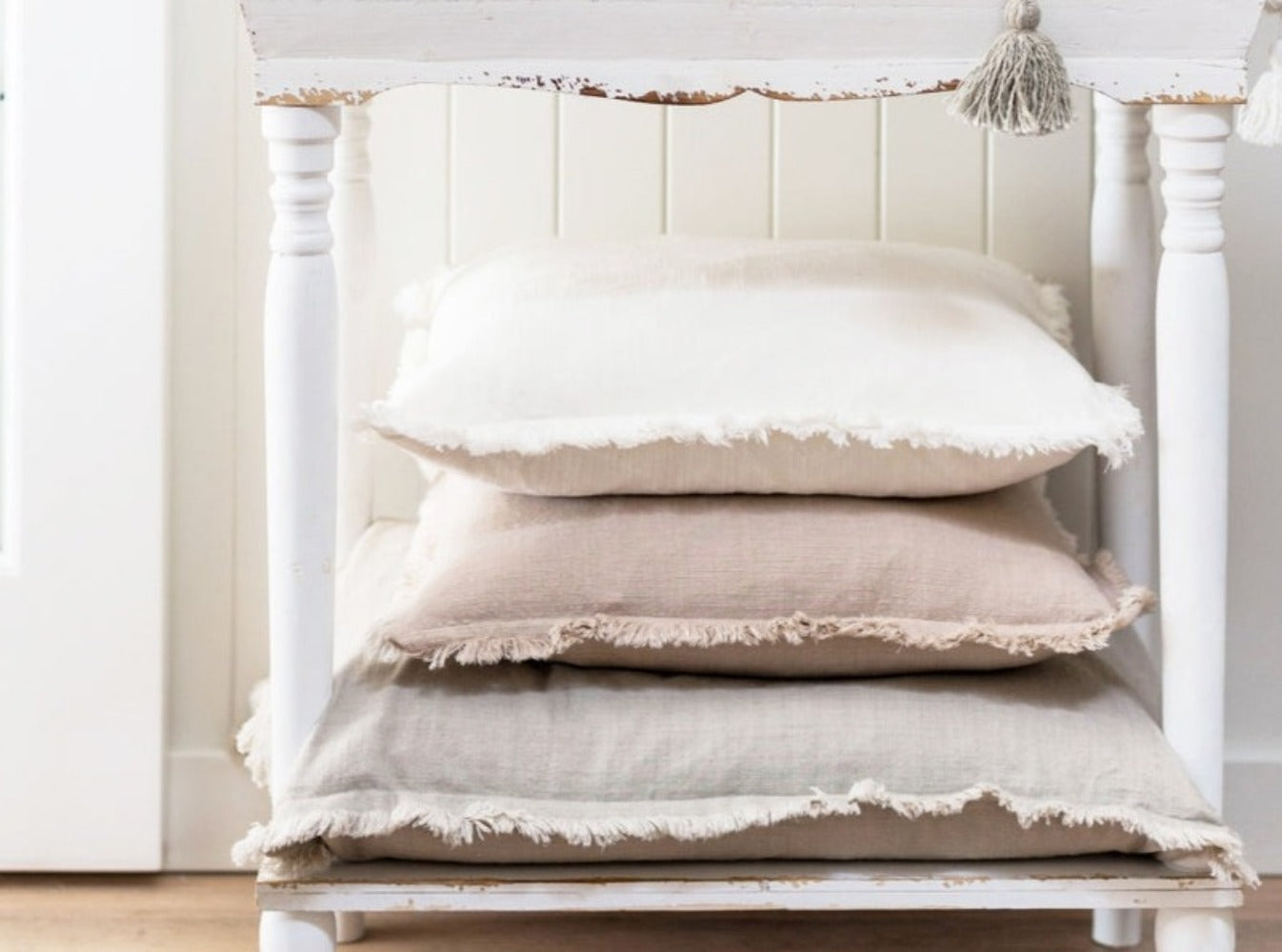 Fringe pillows stacked on table; colors: white, beige, natural