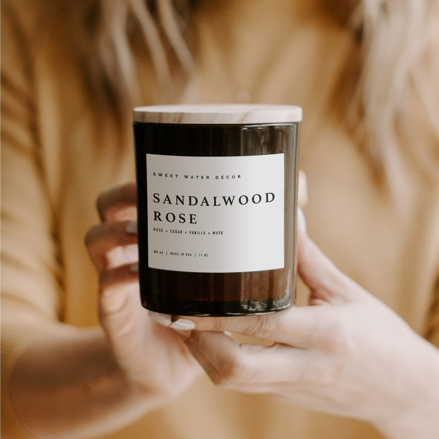 Soy Candle with Wooden Lid in an amber jar. Lady holding in hands an unlit Sandalwood Rose candle.