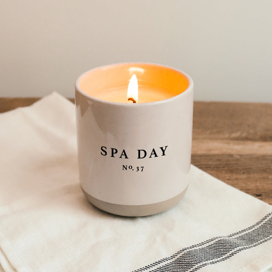 Non-Toxic Soy Candle: Scent: Spa Day.  Stoneware cream colored jar has lit candle on a dish cloth on the table.